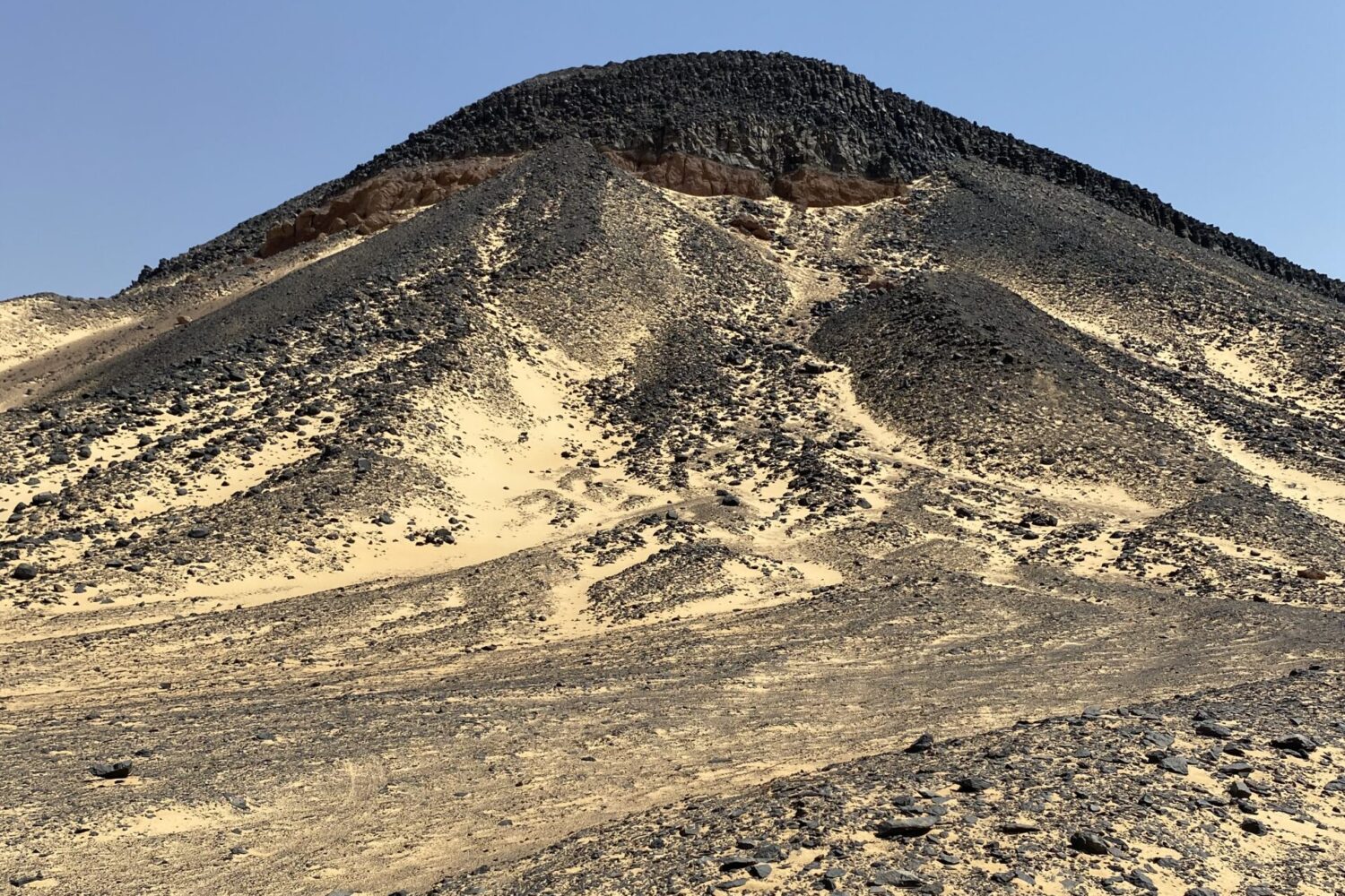 Grandes formações rochosas escuras e cónicas, semelhantes a pequenas montanhas, compostas de pedras vulcânicas pretas no Deserto Negro do Egito