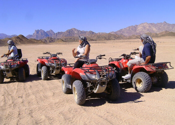 Un groupe de personnes souriantes posant avec leurs quads dans le désert égyptien, prêtes pour un safari