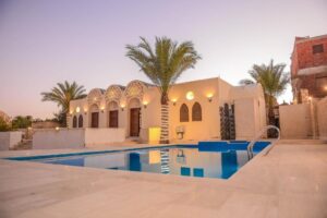 Traditional-style desert villa in Fayoum with arched windows, palm trees, and a serene private swimming pool at sunset.