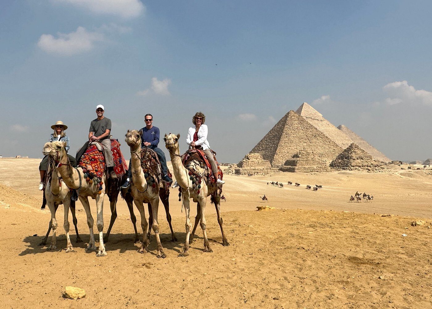 Giza: Aventura Tradicional en Camello, con Vistas Milenarias Una familia montando camellos por el desierto de Giza, con las imponentes pirámides de Egipto visibles en el fondo bajo un cielo despejado