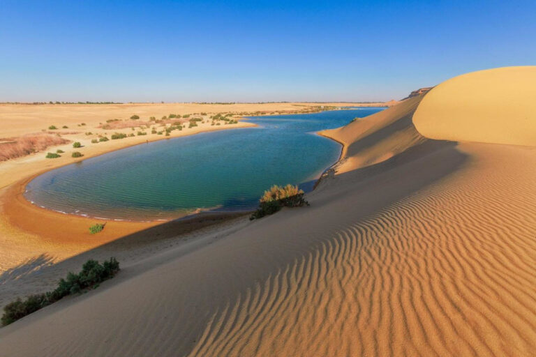 The serene waters of Magic Lake in Fayoum Oasis, showcasing its characteristic color changes from blue to green throughout the day, surrounded by desert dunes
