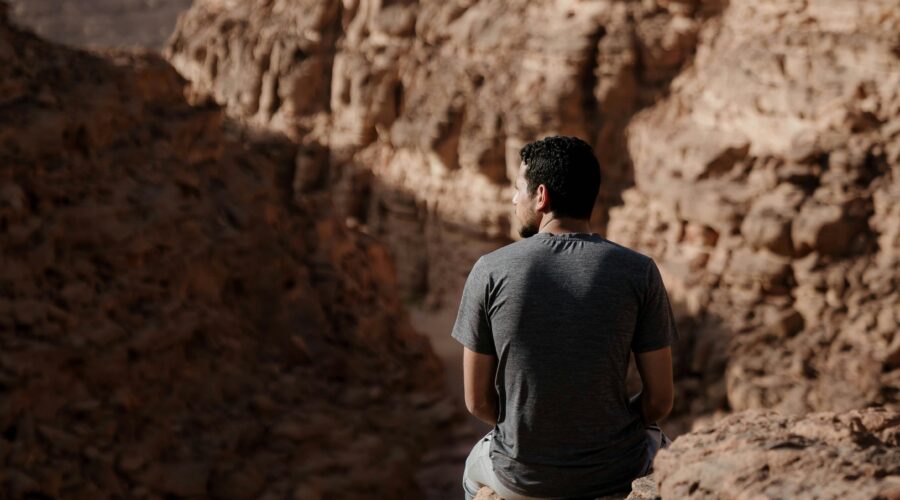 Una persona seduta tranquillamente su una roccia in cima a una montagna del Sinai, contemplando il vasto paesaggio desertico sottostante