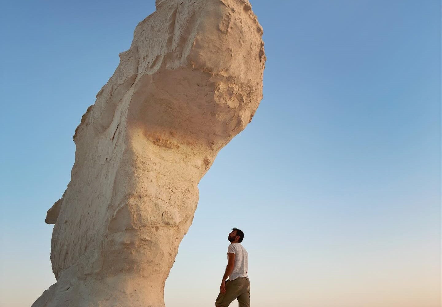 touriste posant près d'une grande formation rocheuse en forme de champignon dans le Désert Blanc, soulignant l'échelle